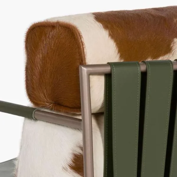 Detail shot of cowhide cushion and olive green leather straps with bronze frame – premium materials on a modern designer chair. صورة قريبة لوسادة جلد البقر وأشرطة جلدية خضراء زيتونية مع إطار برونزي – خامات فاخرة لتصميم كرسي عصري.
