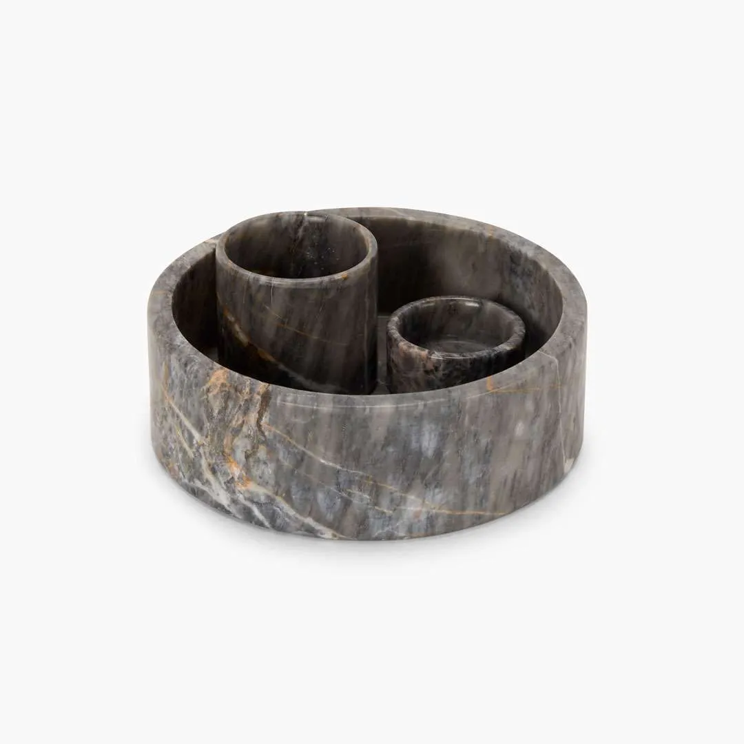Stratus accessory set of 3 carved from luxurious grey marble – modern sculptural home décor for elegant interiors in the UAE. مجموعة ستاتوس من 3 قطع مصنوعة من رخام رمادي فاخر – ديكور منزلي نحتي عصري للمساحات الداخلية الراقية في الإمارات. Elegant marble accessory set displayed on a dark countertop – modern luxury home décor styled with snacks and ceramics in a sophisticated UAE interior. مجموعة إكسسوارات فاخرة من الرخام معروضة على سطح داكن – ديكور منزلي فاخر ومعاصر مزين بوجبات خفيفة وسيراميك في مساحة راقية داخل الإمارات.
