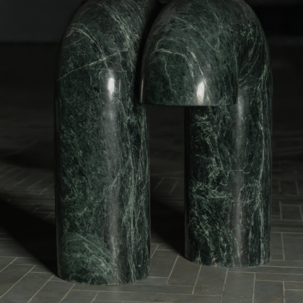 Detail view of the green marble base featuring curved, sculptural legs with a polished finish for a refined dining room centerpiece. لقطة مقربة لقاعدة الطاولة المصنوعة من الرخام الأخضر بأرجل منحنية ولمسة نهائية مصقولة تعكس الفخامة في غرف الطعام.