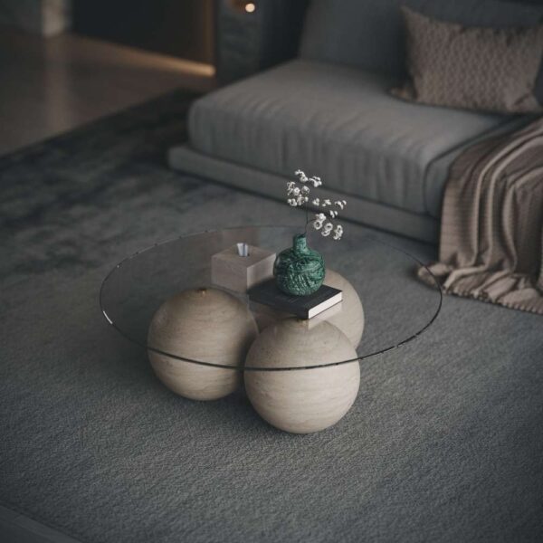 Close-up view of a round glass coffee table with three wooden spheres as base, decorated with a green vase, books, and a tissue box. عرض مقرب لطاولة قهوة دائرية بسطح زجاجي وثلاث كرات خشبية كقاعدة، مزينة بإناء أخضر وكتب وصندوق مناديل.