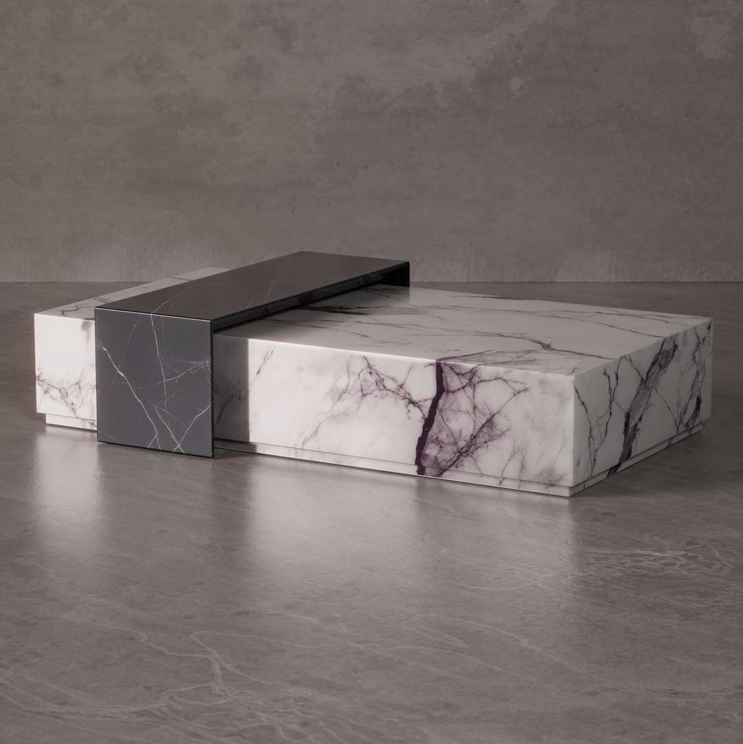 The Marvone Coffee Table features an architectural design composed of intersecting marble volumes. A deep grey marble block overlaps a larger white marble base with purple veining, creating a bold and sculptural centerpiece.