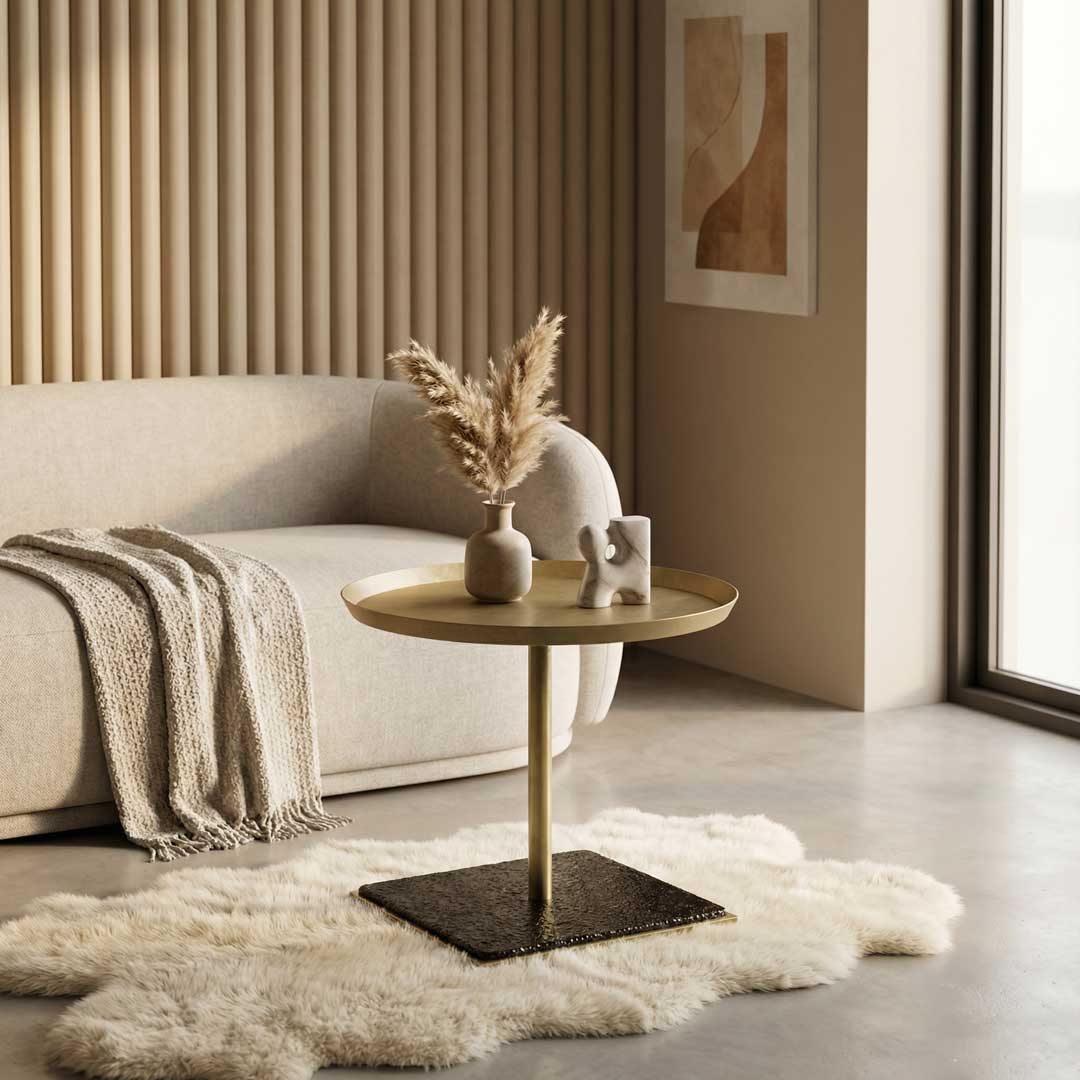 Luxury modern side table with a brushed metal tabletop and sculptural base, styled beside a plush contemporary sofa, showcasing refined designer furniture for elegant living room interiors in Dubai and Abu Dhabi, UAE.