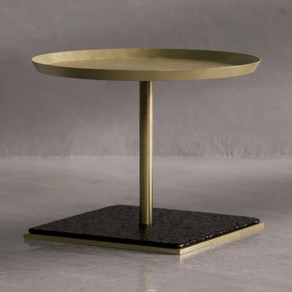 A sculptural side table featuring a hand-hammered brass top, a brushed brass stem, and a square black volcanic stone base. The design combines metallic warmth with organic texture for a refined, modern aesthetic.