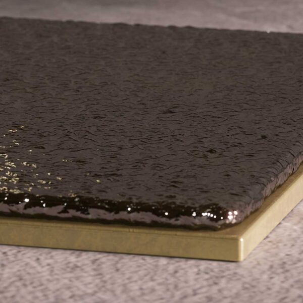A close-up of the Gleam Base Side Table’s base, showing the glossy black volcanic stone surface resting on a brushed brass plate. The tactile contrast highlights the blend of organic texture and metallic sophistication.