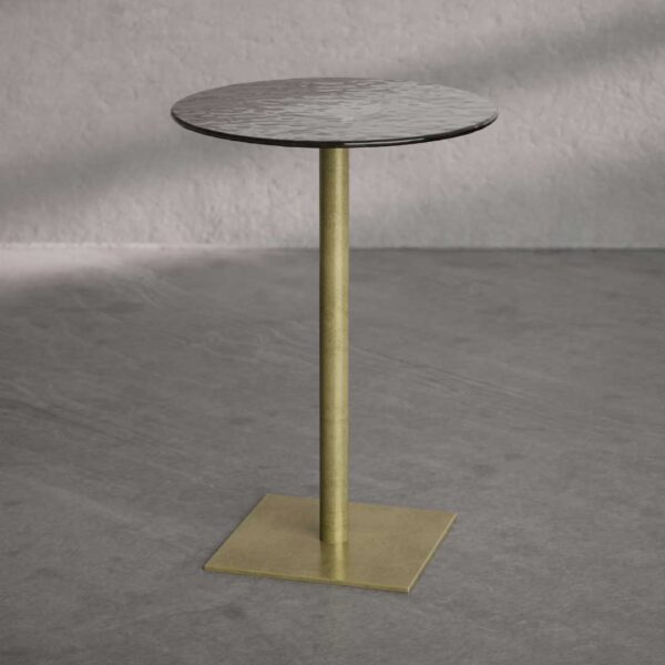 The Virella Side Table features a slender brass-finished stem and a square metal base supporting a round, dark-toned top with a softly textured surface. The minimalist form embodies understated elegance and modern refinement.