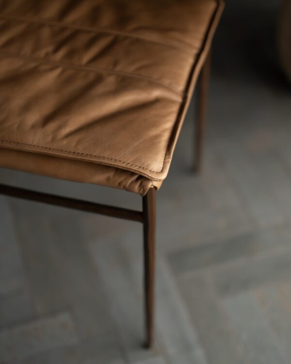 Close-up of the Bon Appétit Dining Chair’s stitched leather seat and slim bronze leg — highlighting refined detailing, smooth upholstery, and the artistry of contemporary furniture design.
